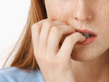 Bliska fotografia młodej kobiety z piegami, która obgryza paznokcie