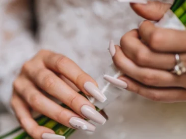 Zbliżenie na dłonie kobiety trzymającej bukiet ślubny, z paznokciami pomalowanymi na jasny różowy kolor i ozdobionymi delikatnymi wzorami