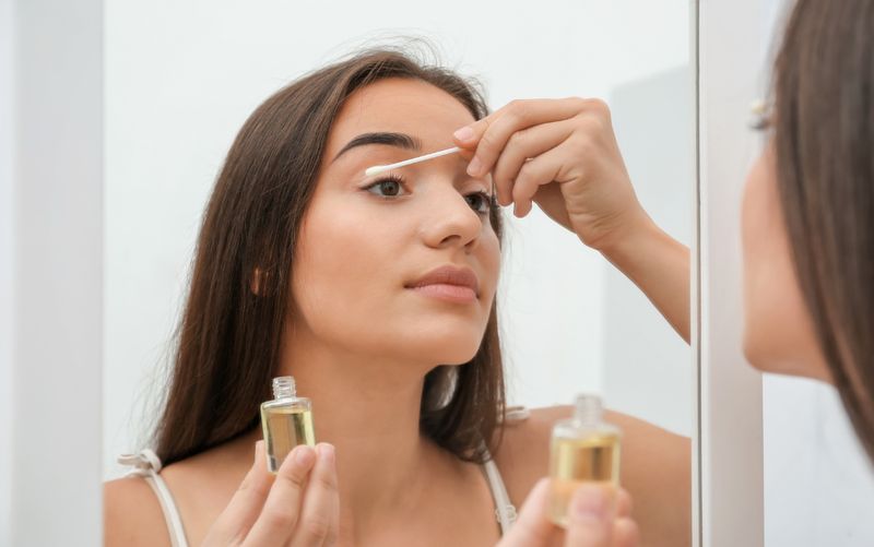 Kobieta nakładająca olejek na rzęsy przed lustrem