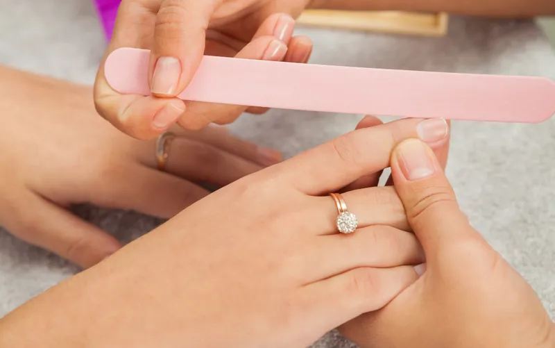 Zdjęcie przedstawia manicure, podczas którego różowy pilnik jest używany do pielęgnacji naturalnie wyglądających paznokci
