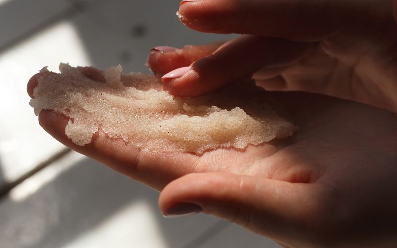 Zdjęcie przedstawia dłoń trzymającą peeling o ziarnistej konsystencji