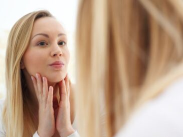 Kobieta patrząca na swoją twarz w lustrze, dotykająca jej dłonią