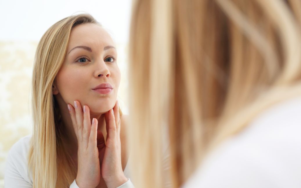 Kobieta patrząca na swoją twarz w lustrze, dotykająca jej dłonią