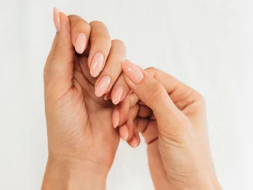 Obraz przedstawia dwie ręce splecione ze sobą, pokazujące manicure w delikatnym, jasnoróżowym kolorze