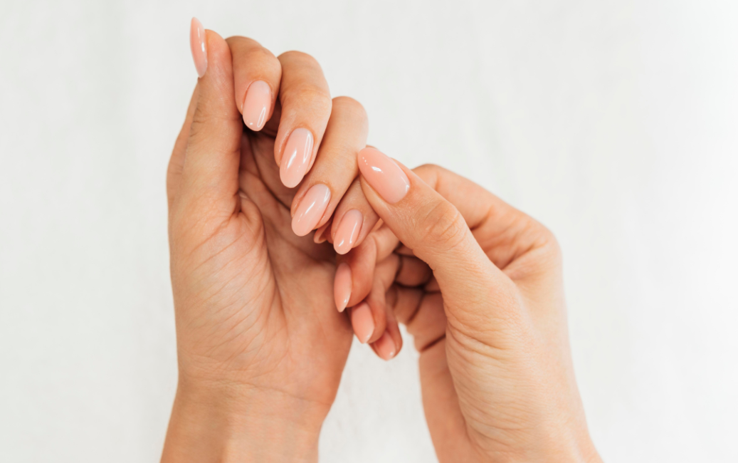 Obraz przedstawia dwie ręce splecione ze sobą, pokazujące manicure w delikatnym, jasnoróżowym kolorze