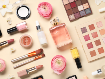 Kosmetyki na jasnym tle: cienie do powiek, lakiery do paznokci, pomadki, pędzle do makijażu, perfumy, róż, puder, krem, kwiaty