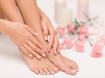 Zadbane stopy i dłonie z różowym lakierem do paznokci, na tle kwiatów i świec, przedstawiające efekt domowej pielęgnacji