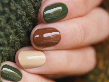 Na zdjęciu widoczne są paznokcie pomalowane w odcieniach ziemi: ciemna zieleń, brąz i jasny beż