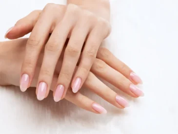 Zadbane dłonie z eleganckim manicure w naturalnym, różowym odcieniu na paznokciach, sfotografowane na jasnym tle