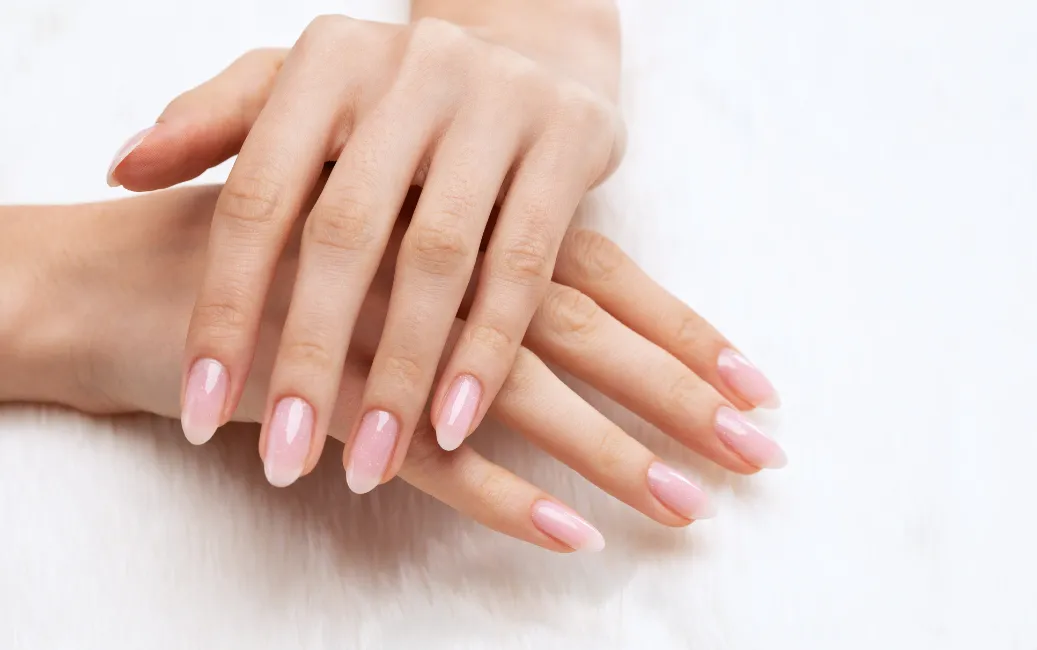 Zadbane dłonie z eleganckim manicure w naturalnym, różowym odcieniu na paznokciach, sfotografowane na jasnym tle