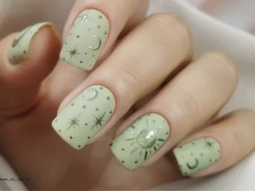 Kwadratowe paznokcie pomalowane na jasny zielony kolor z delikatnymi złotymi zdobieniami w postaci księżyców, gwiazd i słońc