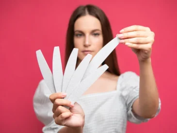 Kobieta trzymająca w dłoniach wachlarz pilników do paznokci na różowym tle