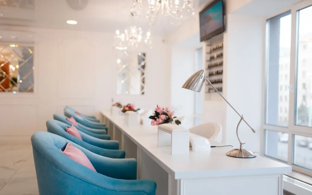Eleganckie wnętrze salonu kosmetycznego z rzędem niebieskich foteli i białymi stanowiskami do manicure